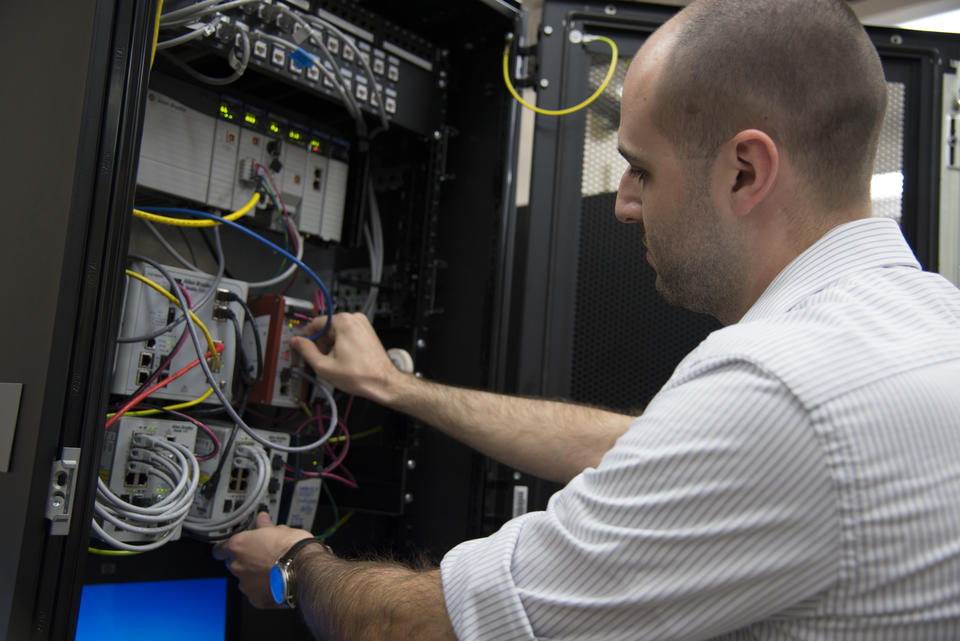 Timothy Zimmerman checking connections in the Cybersecurity for Smart Manufacturing Systems testbed